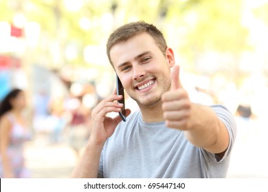 Front View Portrait Of A Guy Calling On Phone Looking At You With Thumbs Up On The Street