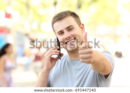 Front view portrait of a guy calling on phone looking at you with thumbs up on the street