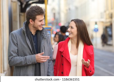 Front view portrait of a happy couple walking in the street having a conversation