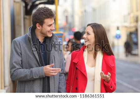 Front view portrait of a happy couple walking in the street having a conversation
