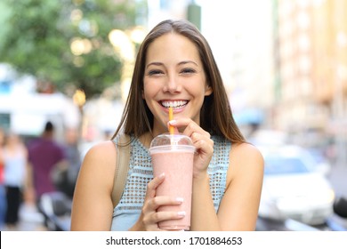 Front view portrait of a happy girl looking camera drinking milkshake in the street - Powered by Shutterstock