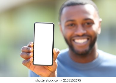 Front view portrait of a happy man with black skin showing blank phone screen outdoors