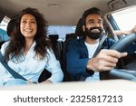 Front view portrait of happy middle eastern man driving modern luxury car and excited young woman sitting on the front passenger seat, looking on the road and smiling