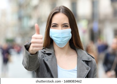 Front View Portrait Of A Happy Woman With Protective Mask Gesturing Thumbs Up In The Street