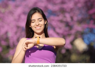 Front view portrait of a happy woman checking smartwatch in a violet park - Powered by Shutterstock