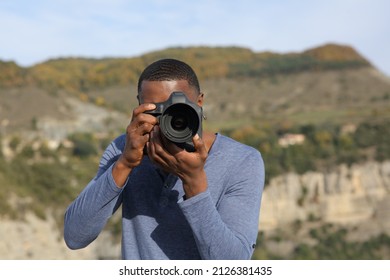 Front view portrait of a man with black skin taking photos with dslr camera in nature