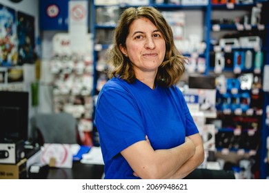 Front View Portrait Of Mature Adult Caucasian One Woman Standing In The Electronics Store Small Business Owner Female Entrepreneur Serious Looking To The Camera Wearing Blue T Shirt Real People