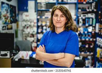 Front View Portrait Of Mature Adult Caucasian One Woman Standing In The Electronics Store Small Business Owner Female Entrepreneur Serious Looking To The Camera Wearing Blue T Shirt Real People