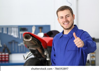 Front view portrait of a motorbike mechanic looking at camera with thumbs up in a mechanical workshop - Powered by Shutterstock