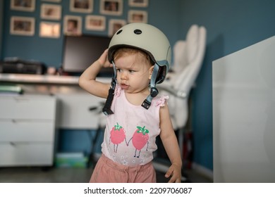 Front View Portrait Of One Girl Small Caucasian Toddler Baby Wear Protective Helmet On Head While Standing Or Walking At Home In Room Growing Up Learning New Skills Early Development Concept