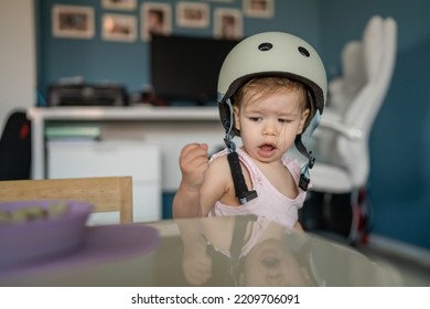 Front View Portrait Of One Girl Small Caucasian Toddler Baby Wear Protective Helmet On Head While Standing Or Walking At Home In Room Growing Up Learning New Skills Early Development Concept