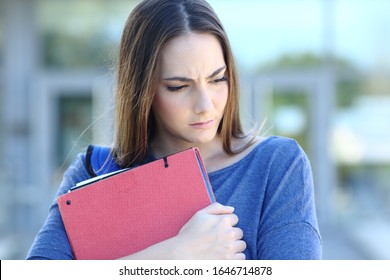 Front View Portrait Of A Sad Student Looking Down Embracing Folders Walking In A College