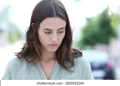 Front view portrait of a sad woman complaining looking down walking in the street - Powered by Shutterstock