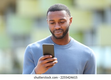 Front view portrait of a serious black man using cellphone in the street - Shutterstock ID 2255424615