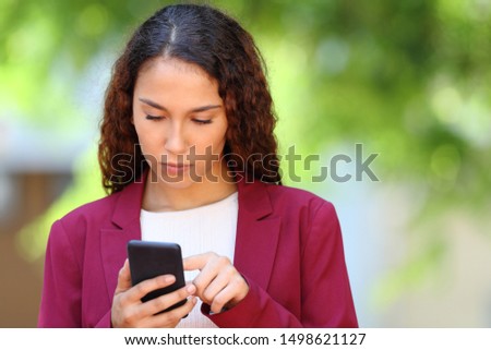Front view portrait of a serious mixed race woman using smart phone on green background