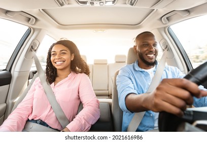 Front View Portrait Of Smiling Handsome African American Man Driving Modern Luxury Car, Happy Beautiful Young Woman Sitting On The Front Passenger Seat, Looking On The Road, Sun Flare