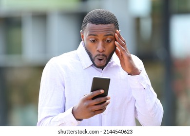Front View Portrait Of A Surprised Man With Black Skin Reading News On Phone In The Street