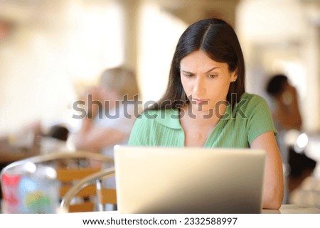 Front view portrait of a suspicious woman using laptop in a restaurant terrace