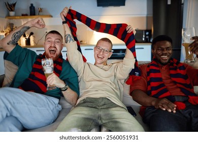 Front view portrait of three adult men watching sports match on TV and cheering with accessories in team colors, copy space - Powered by Shutterstock