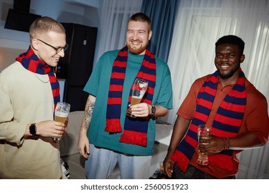 Front view portrait of three smiling sports fans in team colored scarves partying and holding drinks while enjoying victory celebration, shot with flash - Powered by Shutterstock