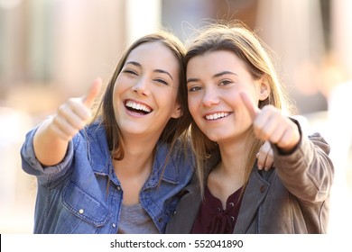 Front view portrait of two funny friends with thumbs up and looking to the camera in the street