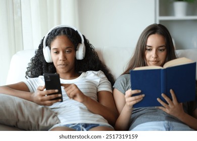 Front view portrait of two interracial roommates one is listening music and the other reads a paper book - Powered by Shutterstock