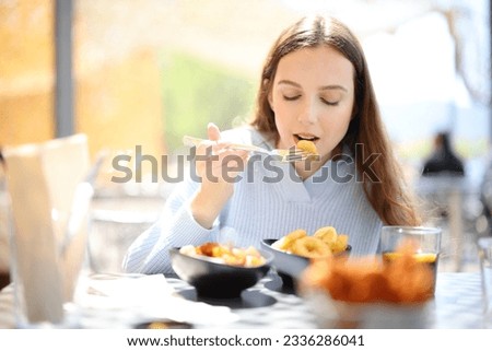 Front view portrait of a woman eating tapas in a bar terrace alone