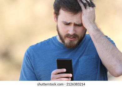 Front view portrait of a worried man checking smartphone outdoors - Powered by Shutterstock