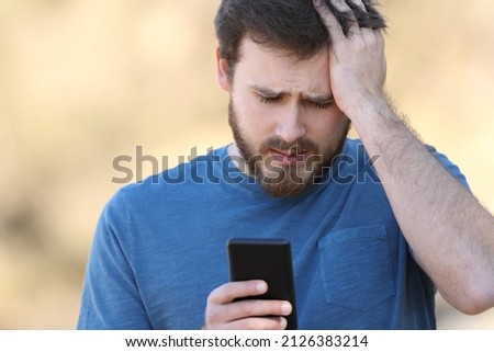 Front view portrait of a worried man checking smartphone outdoors