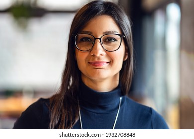 Front View Portrait Of Young Adult Caucasian Happy Joyful Woman With Black Long Hair And Eyeglasses Looking To The Camera While Standing Indoor In Day Real People