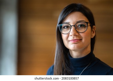 Front View Portrait Of Young Adult Caucasian Happy Joyful Woman With Black Long Hair And Eyeglasses Looking To The Camera While Standing Indoor In Day With Copy Space Real People