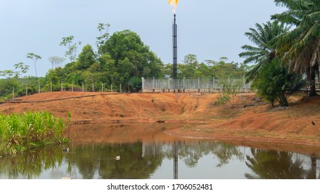Front view of a production natural gas well tower burning gas on top near a lagoon in the middle of the jungle