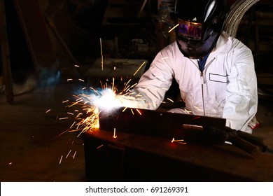 Front view of professional welder in white uniform with protective helmet welding steel with spark in workshop. Industrial worker concept. - Shutterstock ID 691269391