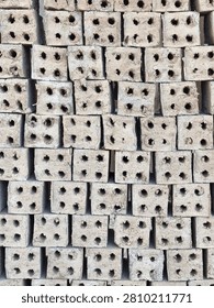 Front view of raw clay bricks with four holes stacked together, background texture of unburned construction materials.