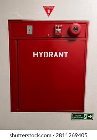 Front view of a red fire hydrant cabinet with emergency fire alarm system installed on an indoor building wall. Fire safety equipment for emergency preparedness and building protection.