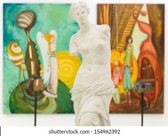 front view of replica of Venus de Milo statue in an art gallery with colorful paintings displayed on walls
