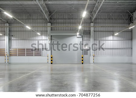 Front view of a roller door (roller shutter) in a dark gray tone, captured in a nighttime scene. The closed shutter functions as a secure entrance to a commercial building, factory, warehouse, or aircraft hangar, emphasizing security, controlled access, and storage protection.

The setting includes a modern industrial interior with a polished concrete floor, clean and reflective, creating a professional environment suitable for commercial and industrial use. The minimal composition, combined with the closed roller shutter, highlights themes of safety, privacy, and restricted entry, which are essential in logistics centers, manufacturing plants, and storage facilities.

This space is ideal for use as a product display background, offering a neutral and structured environment for showcasing automobiles, boats, machinery, heavy equipment, or products. The dark gray tones and low-light atmosphere enhance contrast, depth, and a modern aesthetic, making it suitable for advertising, branding, product presentations, and digital marketing visuals.

The polished concrete floor contributes to a sense of durability, cleanliness, and modern design, often associated with high-end industrial facilities and contemporary commercial spaces. The closed roller door adds a strong visual focal point, symbolizing protection, storage, and industrial functionality.

Overall, this image is well-suited for themes related to design, warehouse interiors, factory environments, logistics and distribution, secure storage, and commercial infrastructure, making it a versatile asset for stock photography, advertising campaigns, and business-related content.
