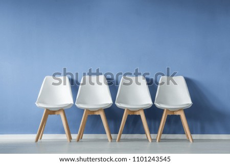 Front view of a row of modern, simple white chairs against blue wall in a minimal style waiting room interior