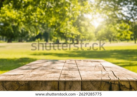 Front view of rustic wooden table with blurred green park trees and bright sunlight in background. Natural outdoor setting. Picnic or food mockup