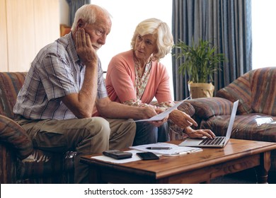 Front View Of Sad Caucasian Senior Couple Discussing Bill While Sitting On Vintage Sofa At Retirement Home. Senior Woman Is Using Laptop.