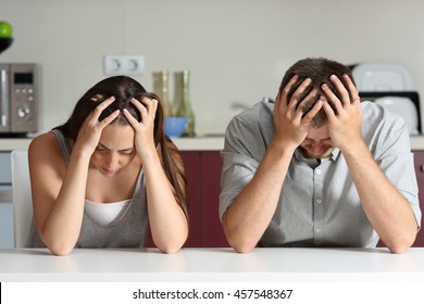 Front View Of A Sad Couple With Hands On Head Sitting In The Kitchen Of A House