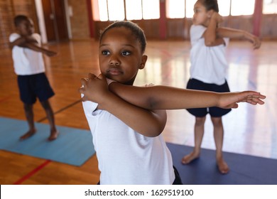 Front view of schoolgirl doing yoga stretch on a yoga mat in school - Powered by Shutterstock