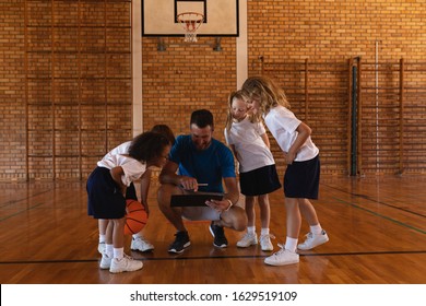 Front view of schoolkids looking at clipboard at basketball court in school - Powered by Shutterstock