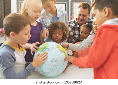 Front view of a schoolteacher discusing over a earth globe in classroom at school with his school kids - Powered by Shutterstock