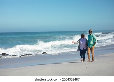 Front view of a senior African American couple walking on the beach with blue sky and sea in the background, holding hands and talking, the woman gesturing with her hand - Powered by Shutterstock