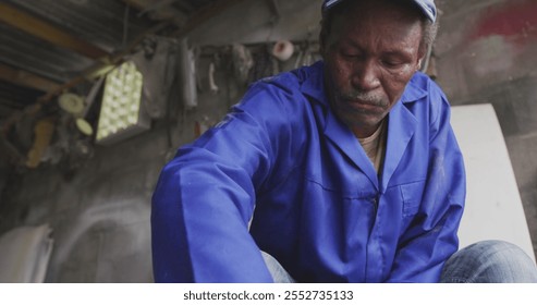 Front view of a senior African male panel beater in a township workshop, cleaning an alloy whee. Shot in Capetown South Africa. - Powered by Shutterstock