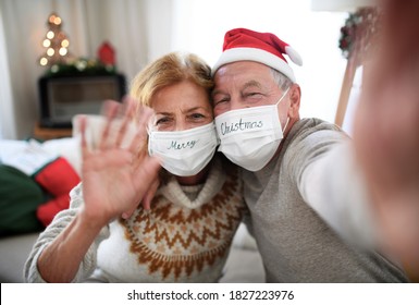 Front view of senior couple with face masks indoors at home at Christmas, taking selfie.