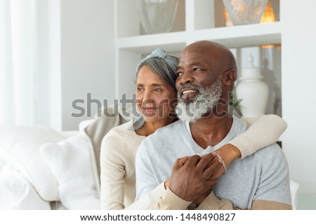 Front view of senior diverse couple sitting on a white couch in beach house. Authentic Senior Retired Life Concept