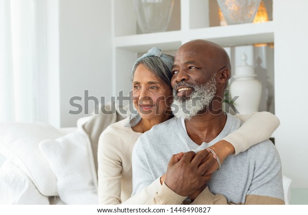Front view\
of senior diverse couple sitting on a white couch in beach house.\
Authentic Senior Retired Life\
Concept