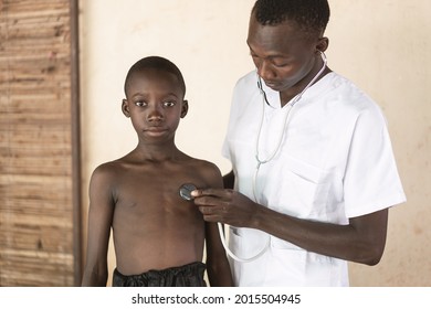 Front View Of A Serious Black Healthcare Worker Examinating Lung And Heart Sounds Of A Bare Chested African Schoolboy By The Means Of A Stethoscope In A Village Hospital